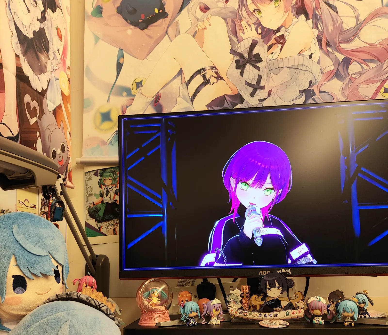 A desktop monitor streaming the SHINier live, showing Tokoyami Towa singing on stage, watched from a desk crowded with plush toys and figurines